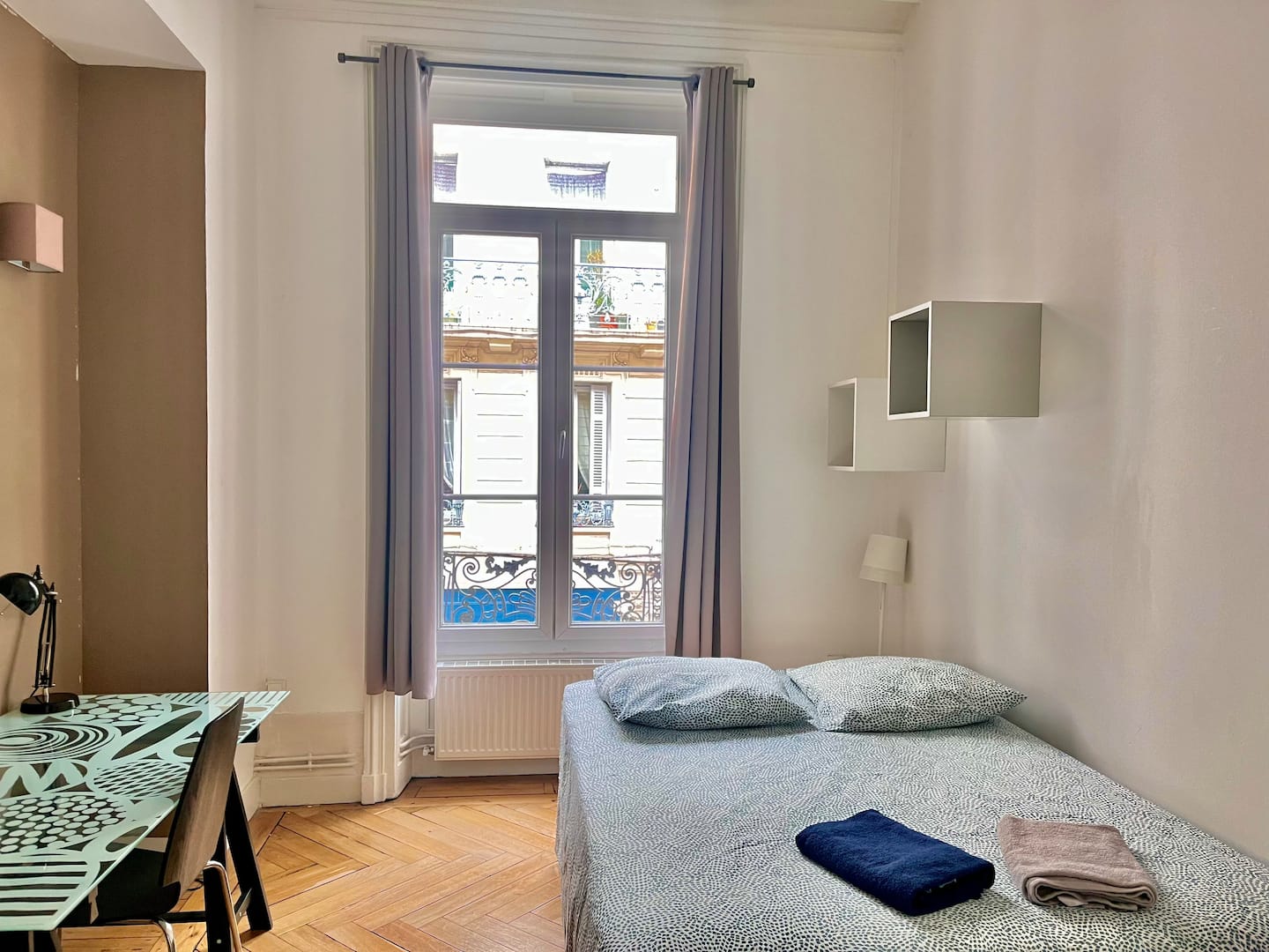 Chambre 2 avec lit double gris, bureau à gauche et grande fenêtre aux rideaux gris