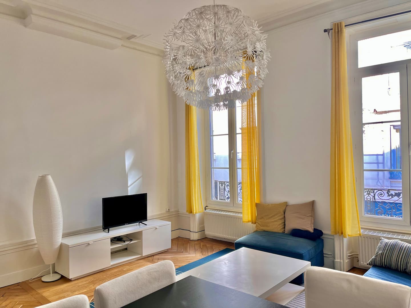 Séjour du Central avec télévision, table basse et grandes fenêtres aux rideaux jaunes